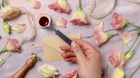 Hands pouring melted wax onto an envelope near pink flowers