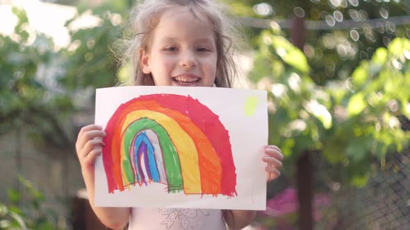 Happy Little Girl Holding a Children's Rainbow Drawing