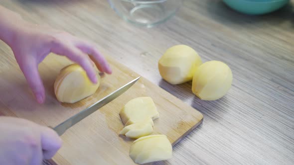 Woman is Finely Slicing Young Fresh Potatoes in the Kitchen with Sharp Knife on Wooden Board for