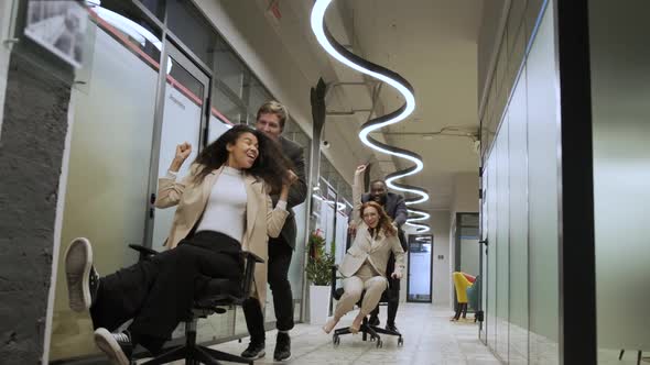 Millennial Multiracial Team People Having Fun Riding on Chairs in Office Room Excited Diverse