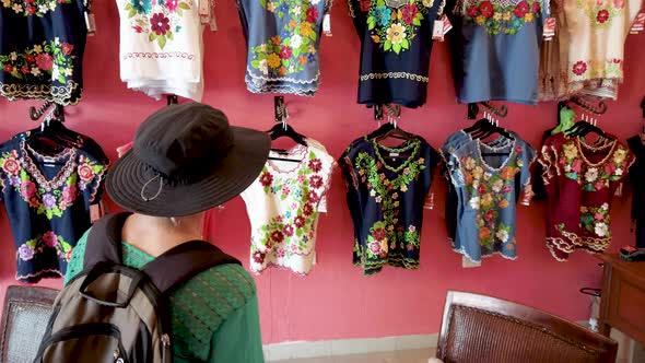 Woman tourist looks at fashionable designer huipil blouses in Merida, Mexico.