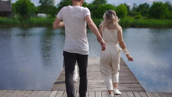 Tracking Shot of Excited Young Couple Running in Slow Motion to River on Wooden Pier Smiling