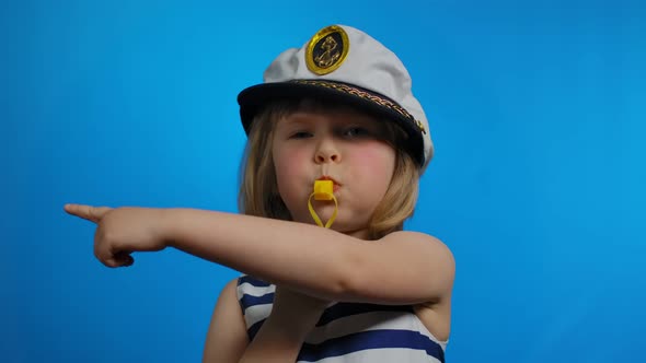 Little Girl in a Sailor Hat is Blowing in a Whistle and Pointing to the Side