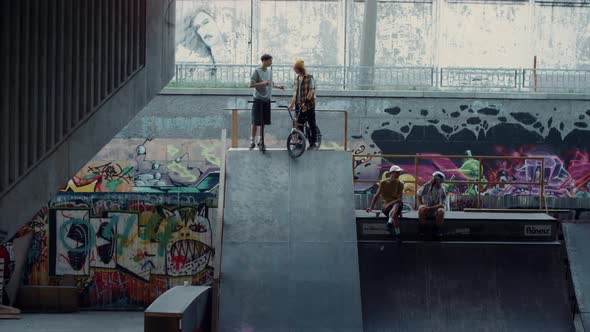 Young Guys Communicating Together in Skate Park with Graffiti Wall