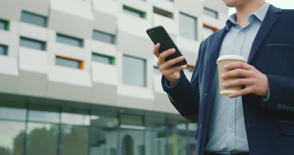 A Businessman is Walking Near the Business Center with a Cup of Coffee in His Hand