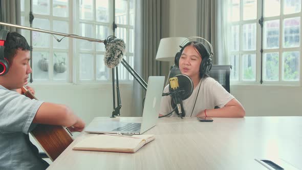 Kid Girl In Headphones Singing Into Microphone While Boy Playing The Guitar During Online Livestream