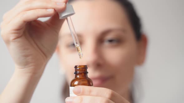 Close Up of Female Young Caucasian Woman Opens Bottle with Skin Care Oil Dropper