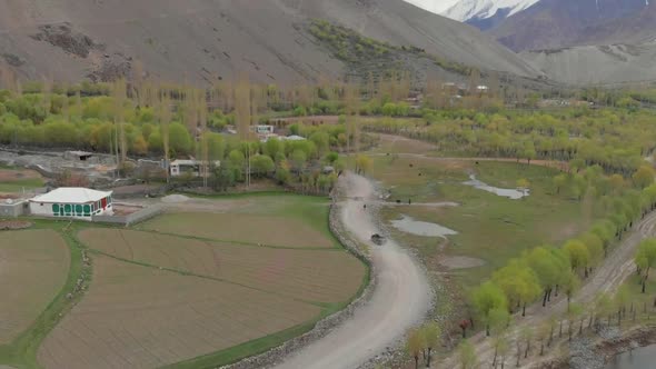 Aerial Over Local Ghizer Valley Village In Pakistan With Car Driving Through. Follow Shot