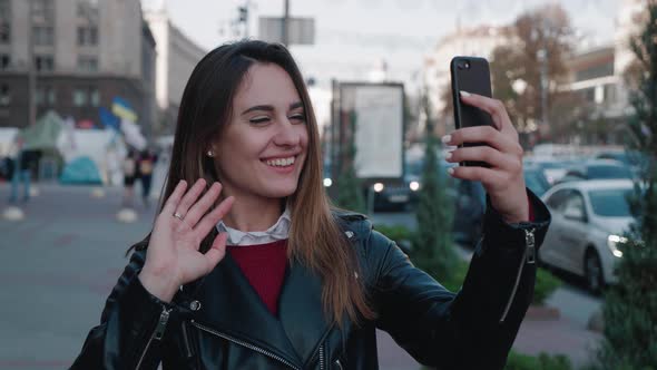 A Lovely Smiling Brunette Woman is Talking to Someone with a Video Chat While Standing in the Square