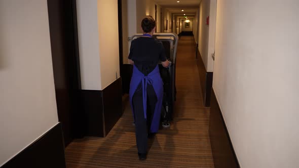 Cleaning Lady Driving Trolley Down Hotel Corridor