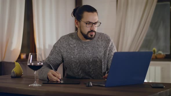 A Young Handsome Man in Glasses Works on a Laptop