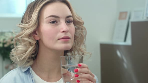 Gorgeous Young Woman Is Keeping Healthy By Drinking a Glass of Water Indoors and Smiling