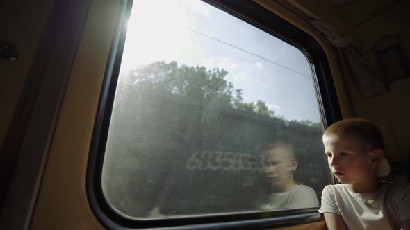 Kid looks out the train window. Boy is traveling by train. Oncoming freight train outside