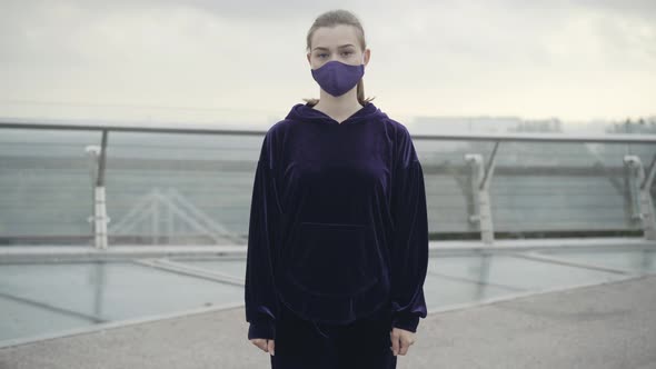 Serious Young Sportswoman in Covid19 Face Mask Standing Outdoors Looking at Camera