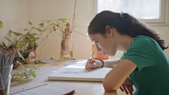 Teenage artist sitting drawing in a sketchbook in her room