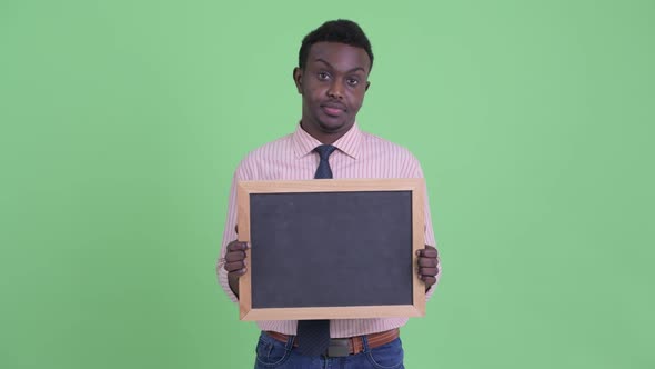 Stressed Young African Businessman Holding Blackboard