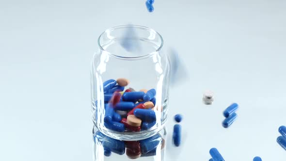 Colorful Pills Fall Down Into a Bottle, on White, Reflection