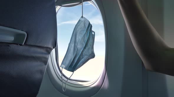 Disposable Mask Hangs on Woman Finger Against Plane Window