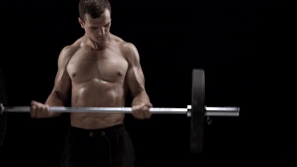 Man is Doing Exercises with a Barbell Training on a Black Background in the Studio