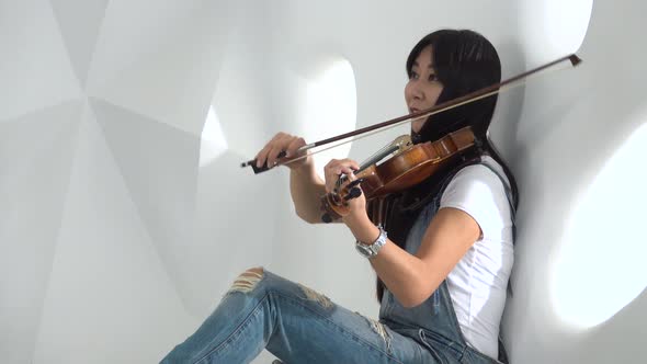Girl of Asian Appearance Sitting on the Floor Playing a Violin