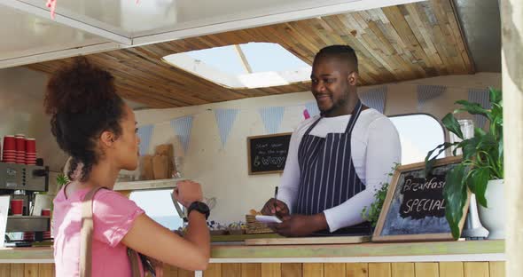 Smiling african american male food truck owner taking order from happy female customer