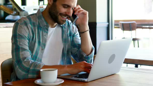 Man talking on mobile phone while using laptop