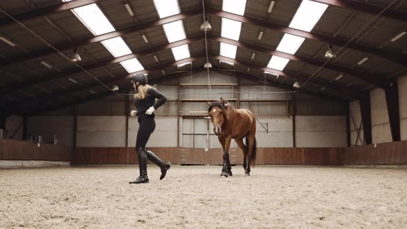 Woman Running Through Paddock With Horse Following