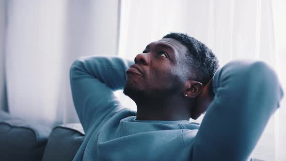 Serious Man Thinking While Sitting on a Blue Sofa  Hands Behind the Head