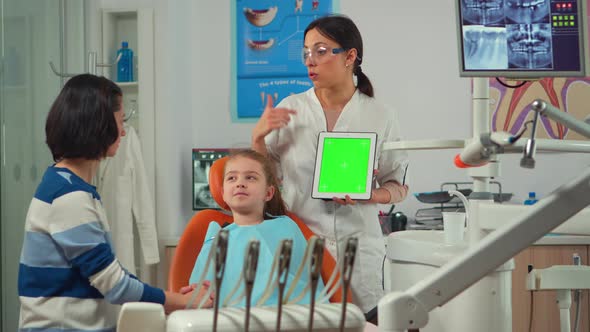 Pediatric Dentist Standing Near Girl Patient Pointing at Green Screen Display