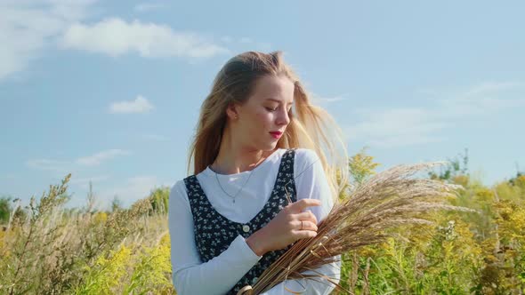A Young Girl in a Beautiful Dress Walks Through a Field with Spikelets and Wheat