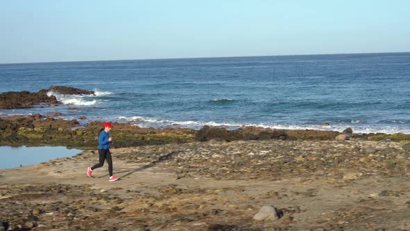Woman Runs Along the Stony Shore of the Ocean