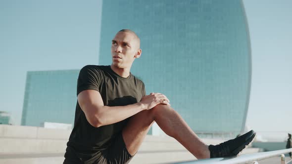 Confident bald sportsman wearing black t-shirt doing stretching exercise outdoors