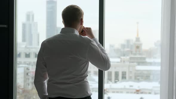 businessman with a mug of coffee stands by the window overlooking the city