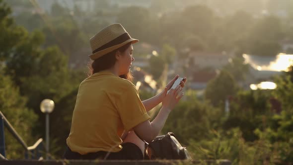 A woman sits on the street and uses her smartphone. Rear view.