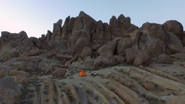 Aerial shot of a young man backpacker camping with his dog in a mountainous desert.