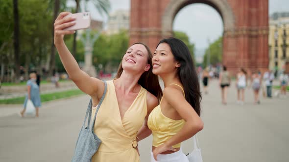 Two Young Lovely Diverse Female Friends Taking Picture on Cellphone Outdoors Near Historic Building