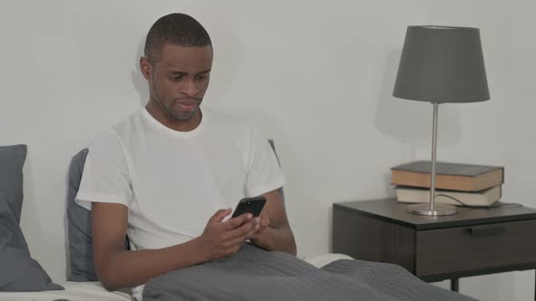 African Man Using Smartphone Sitting in Bed