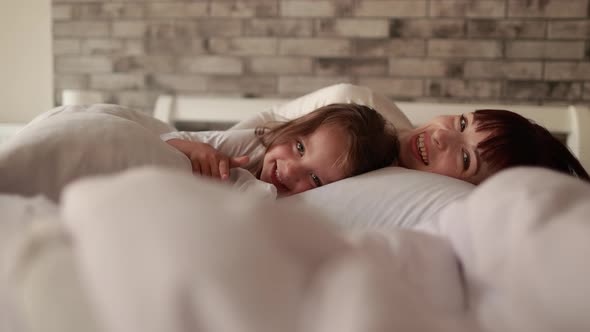 Mother and Baby Playing and Smiling While Lying on a White Blanket