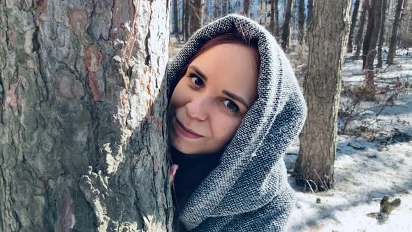 Young Woman in Gray Coat Looking Out of Tree in Forest
