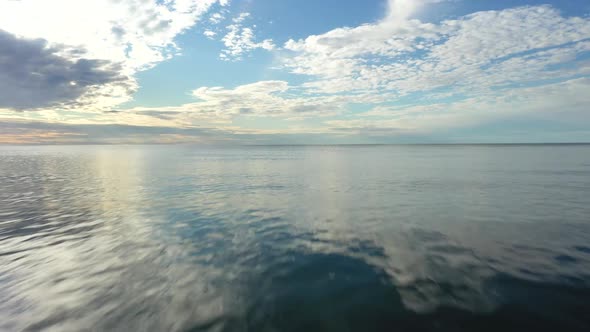 AERIAL: Flying Very Low Above the Surface of Sea into the Horizon with Blue Cloudy Sky