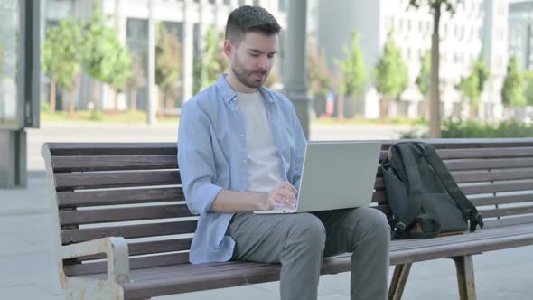 Young Man with Back Pain Using Laptop While Sitting on Bench
