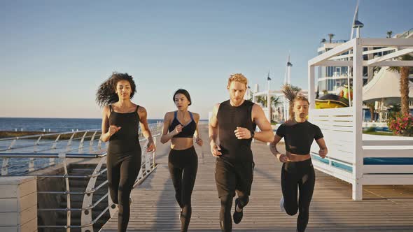 Muscular Man Couch Running with Three Diverse Sporty Ladies on Pier Warming Up Before Strength