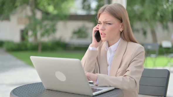 Angry Young Businesswoman Talking on Phone in Outdoor Cafe