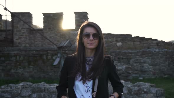 Gorgeous Brunette with Sunglasses Smiling and Posing Against Medieval Stronghold in the Background