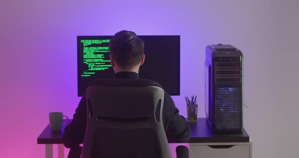 Rear View of Man Programmer Coding Network Security Software Indoors in Neon Lights at Night