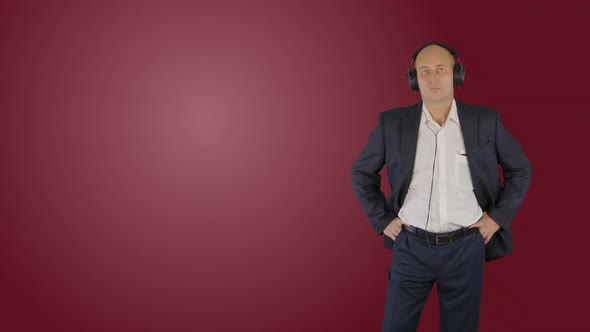 Happy Man in Business Suit Listening Music in Headphones on Red Background