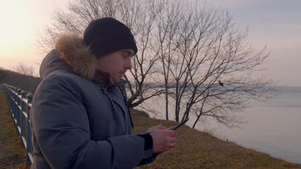 Man Typing Messages on His Smartphone Standing on the Seashore