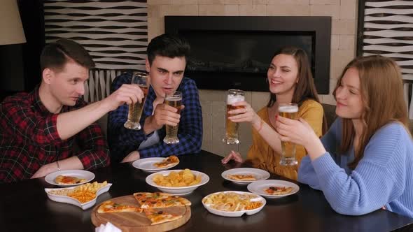 Four Friends Are Relaxing in a Pub, Clinking Glasses of Lager and Eating Pizza