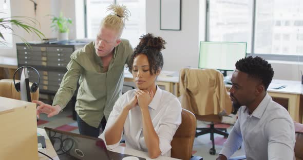 Diverse business people discussing with laptop in creative office