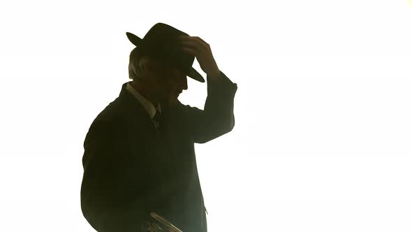 Silhouette of Man Puts on Hat and Starts Playing Trumpet in Smoky Room Side View